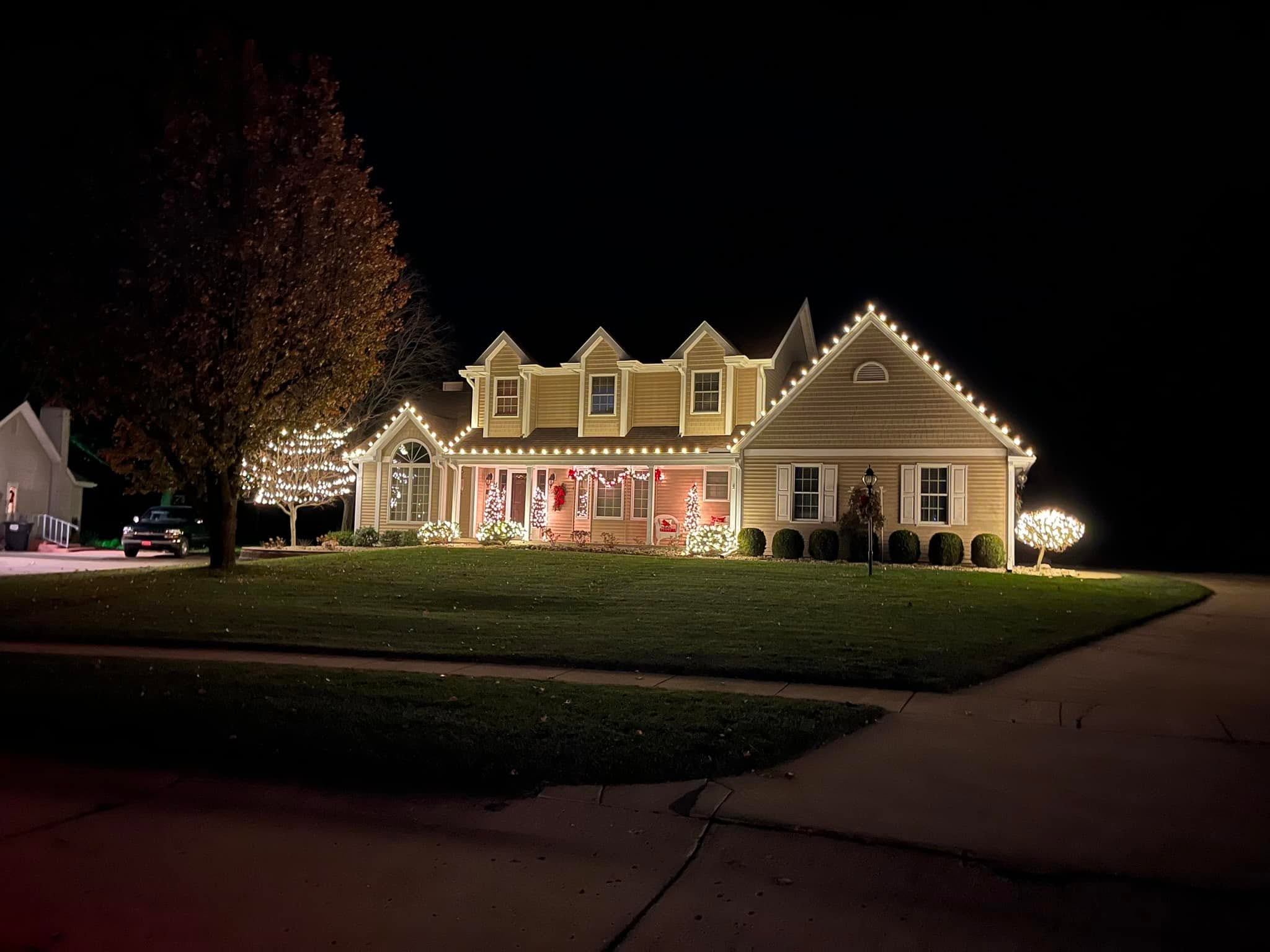 Two-storey home outlined in warm white C9 Christmas lights with a wrapped tree in the yard