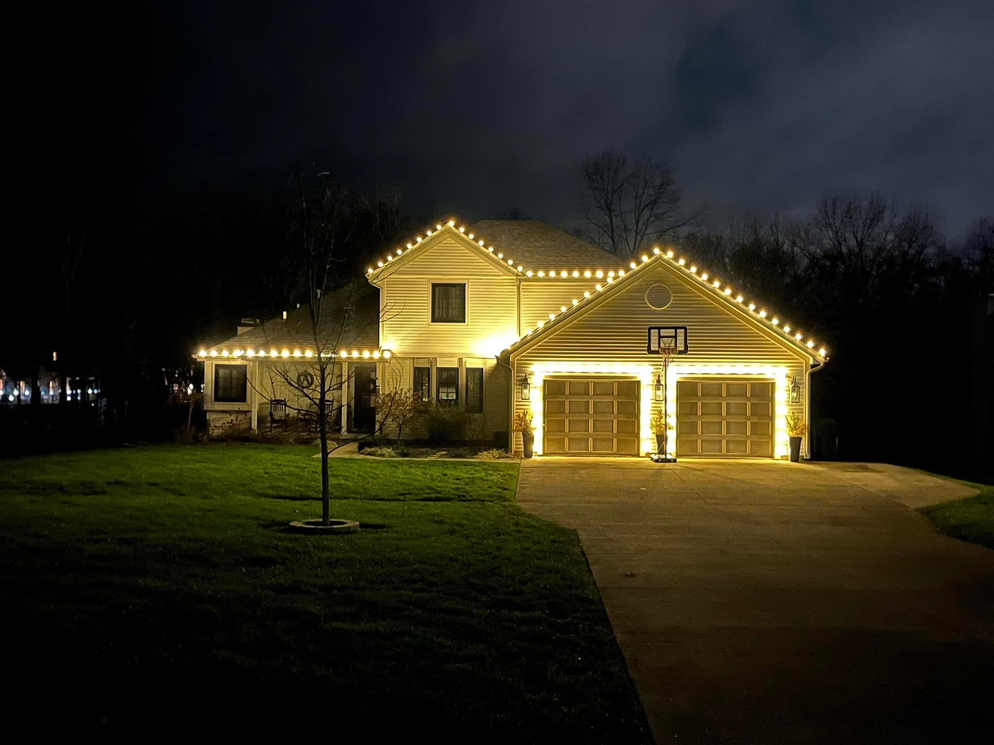 Colonial home with warm white roofline and lit trees